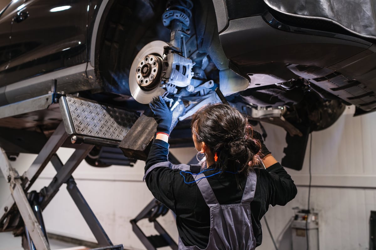 Female mechanic working under a car on hydraulic lift