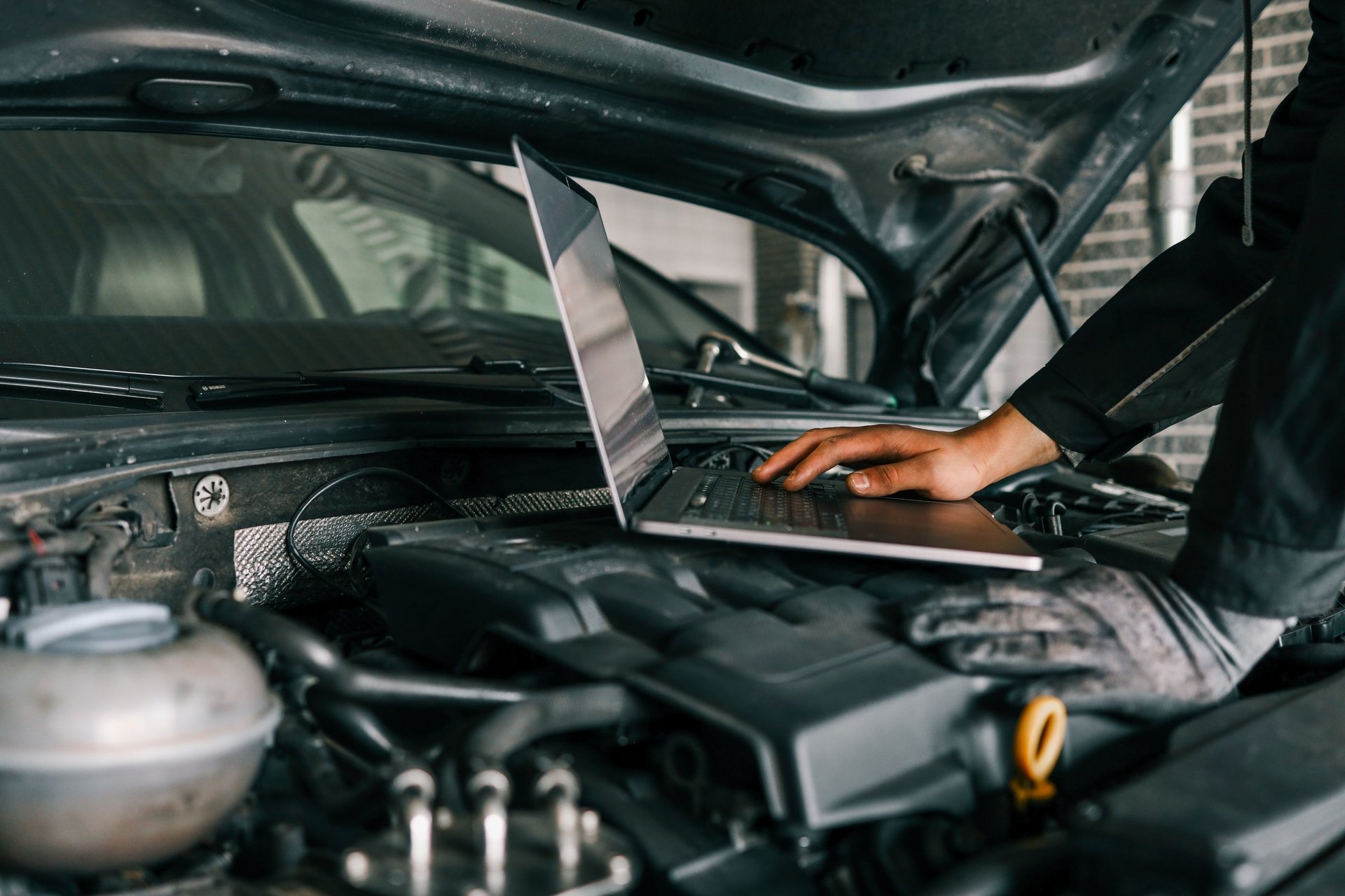 Mechanic using laptop for diagnostics on car engine