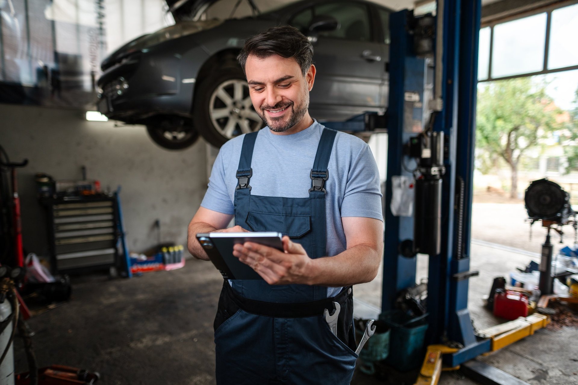 Mechanic using digital tablet next to car on hydraulic lift
